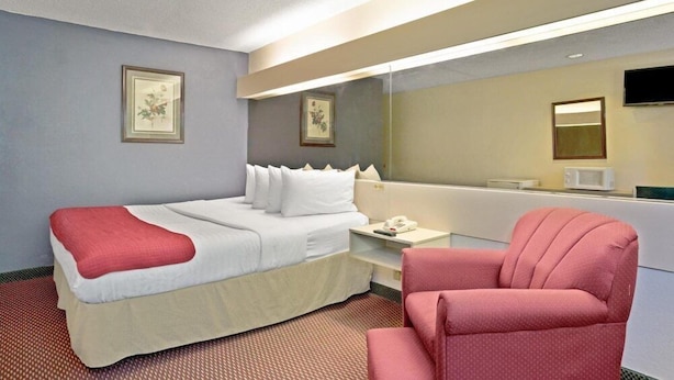 A hotel room with a bed, a chair, a bedside table with a phone, and a mirror.