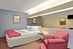 A hotel room with a bed, a chair, a bedside table with a phone, and a mirror. - Microtel Inn & Suites by Wyndham Union City/atlanta Airport (Union City)