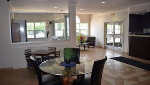 A hotel lobby with a glass table, chairs, a potted plant, and a reception desk.