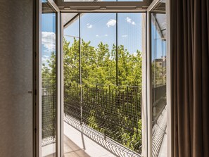 Vista a través de una puerta de cristal con valla de metal, que da a un balcón con suelo de baldosas.