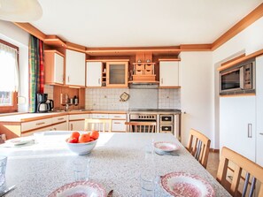 A kitchen with wooden cabinets, a granite countertop, a dining table with chairs, and a bowl of fruit. - Beautiful private villa for 13 guests with WIFI, TV and terrace (Fügen)