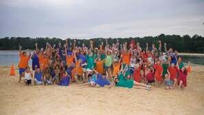 A group of people on a sandy beach with a body of water and trees in the background. - Callaway Gardens (Pine Mountain)