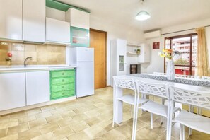 Een moderne keuken met witte kastjes, een groene vaatwasser, en een eethoek met witte stoelen en een tafel.