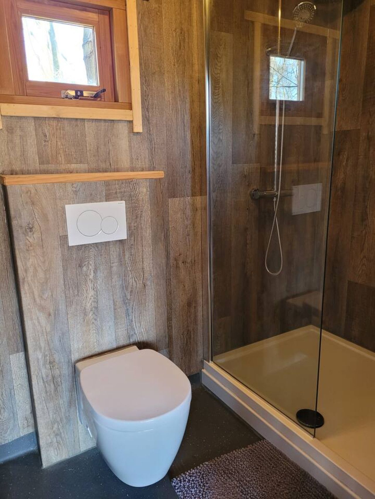 A modern bathroom with a glass-enclosed shower, a white toilet, and a wooden vanity with a built-in light.