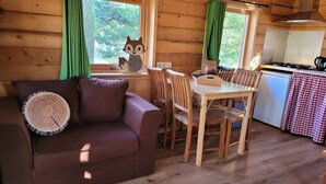 A cozy cabin interior with a wooden floor, a brown leather sofa, a dining table with chairs, and a kitchen area.