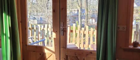 A wooden cabin with a large sliding door, a wooden deck outside, and a doormat on the floor.