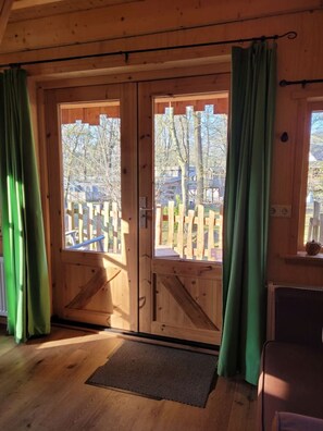 A wooden cabin with a large sliding door, a wooden deck outside, and a doormat on the floor.