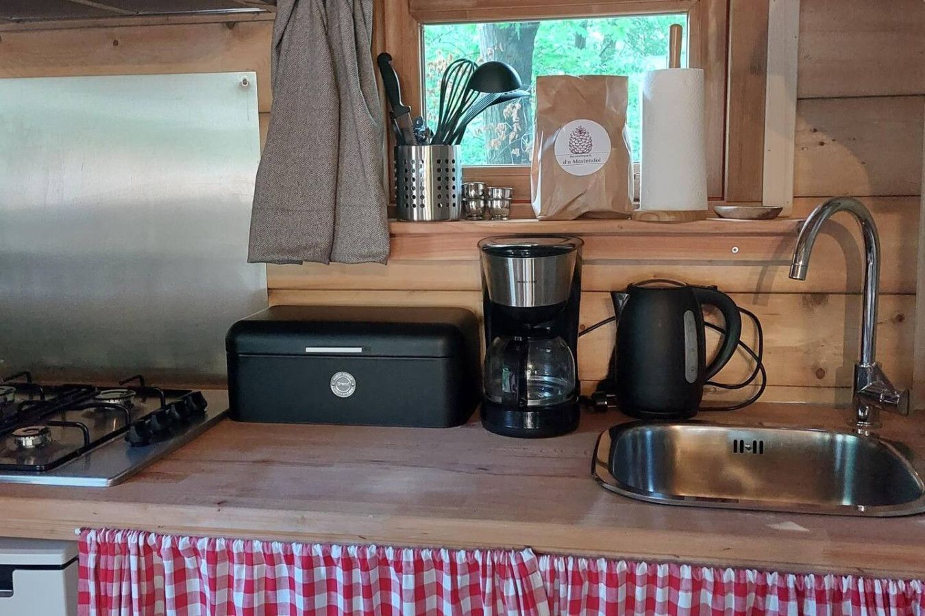 A compact kitchen with a gas stove, a coffee maker, a kettle, and a sink.