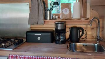A compact kitchen with a gas stove, a coffee maker, a kettle, and a sink.