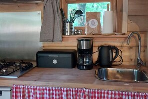 A compact kitchen with a gas stove, a coffee maker, a kettle, and a sink.