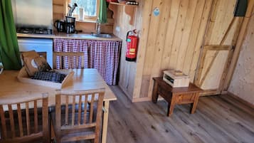 Een houten cabin met een keukenhoek, een eettafel met stoelen en een kleine houten tafel met een doos.
