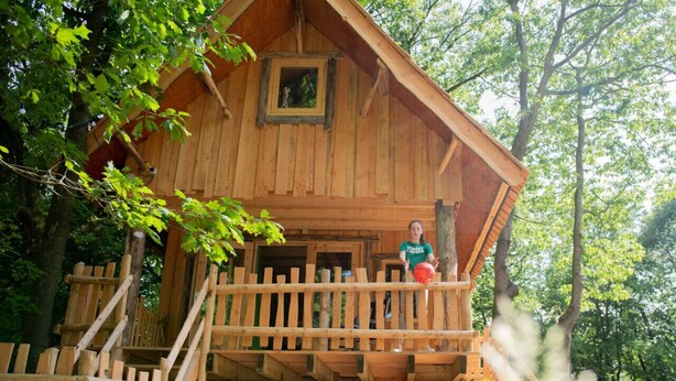 A wooden treehouse with a balcony, surrounded by trees.