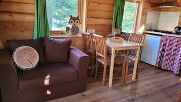 A cozy cabin interior with a wooden floor, a brown leather sofa, a dining table with chairs, and a kitchen area.