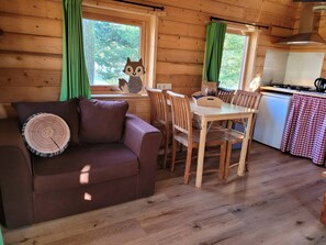 A cozy cabin interior with a wooden floor, a brown leather sofa, a dining table with chairs, and a kitchen area. - Wooden Lodge | Boomhut op d`n Mastendol | Rijen, Brabant (Rijen)