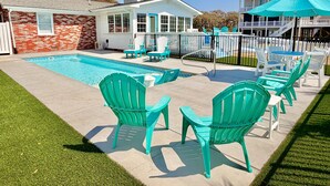Un patio trasero con piscina, sillas de exterior y una zona de estar techada.