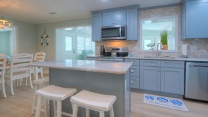 Una cocina con una isla central, taburetes de bar, microondas y un lavamanos.