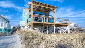 Une maison située en bord de mer, dotée d’une terrasse en bois, d’un balcon et offrant une vue sur l’océan.