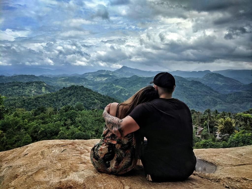 A couple sitting on a rock overlooking a mountainous landscape.