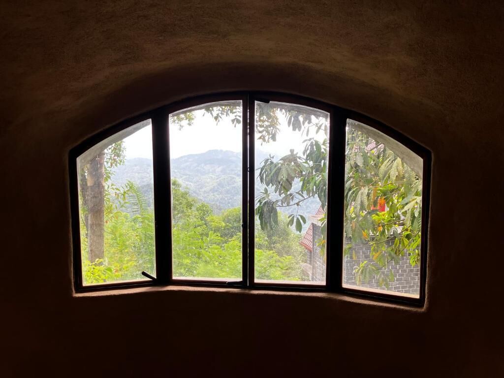 A curved window with a view of lush greenery and distant hills.