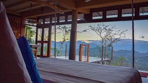 A bedroom with a large bed, a view of mountains, and a dining area with a table and chairs. - The Cloud Resort (Kadugannawa)