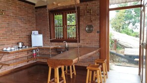 A kitchen with a long wooden bar, stools, a refrigerator, and a hanging pot rack. - The Cloud Resort (Kadugannawa)