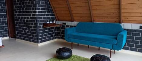Ein Zimmer mit einem blauen Sofa, schwarzen Ziegelwänden und einer Holzbalkendecke.