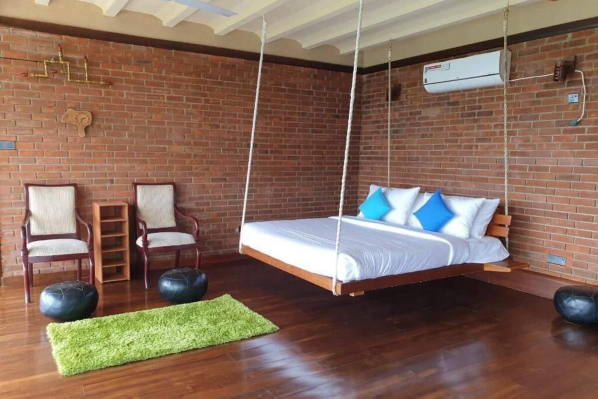 A room with a hanging bed, brick walls, wooden flooring, and a green rug.