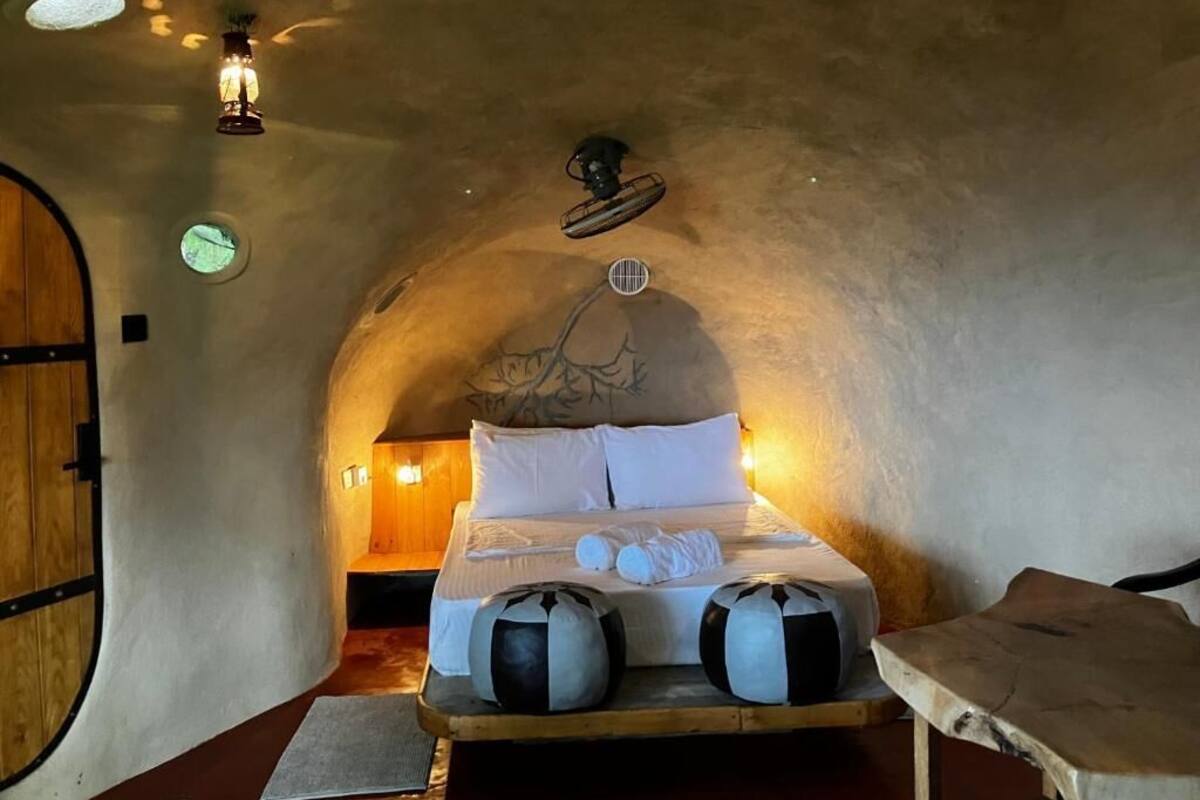 A cozy, circular room with a bed centered in the space, a wooden bench, and a small table.