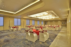 A large conference room with round tables, white chairs, and red tablecloths. - Marigold Regency (Rahata)