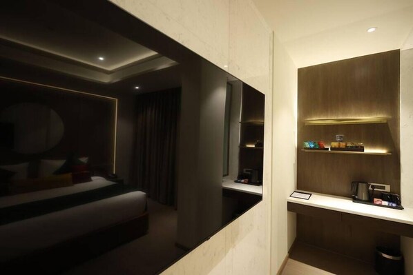 A modern hotel room with a bed, a desk, and a built-in minibar.