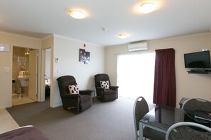 A living room with two armchairs, a glass coffee table, a TV mounted on the wall, and a large window with curtains. - B K S Motor Lodge (Palmerston North)