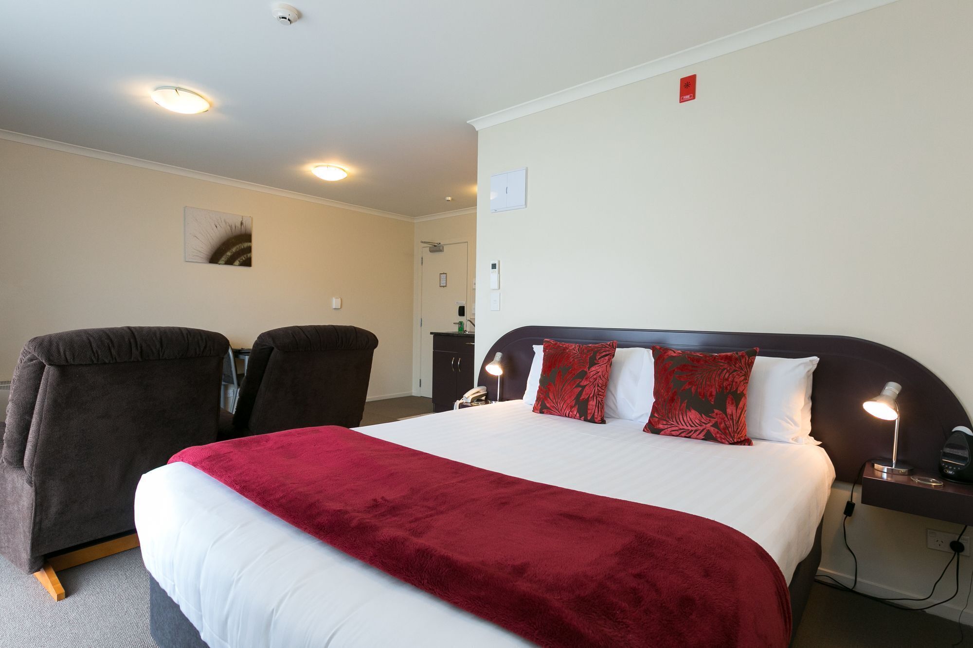 A hotel room with a large bed, two armchairs, a desk, and a nightstand with a lamp.