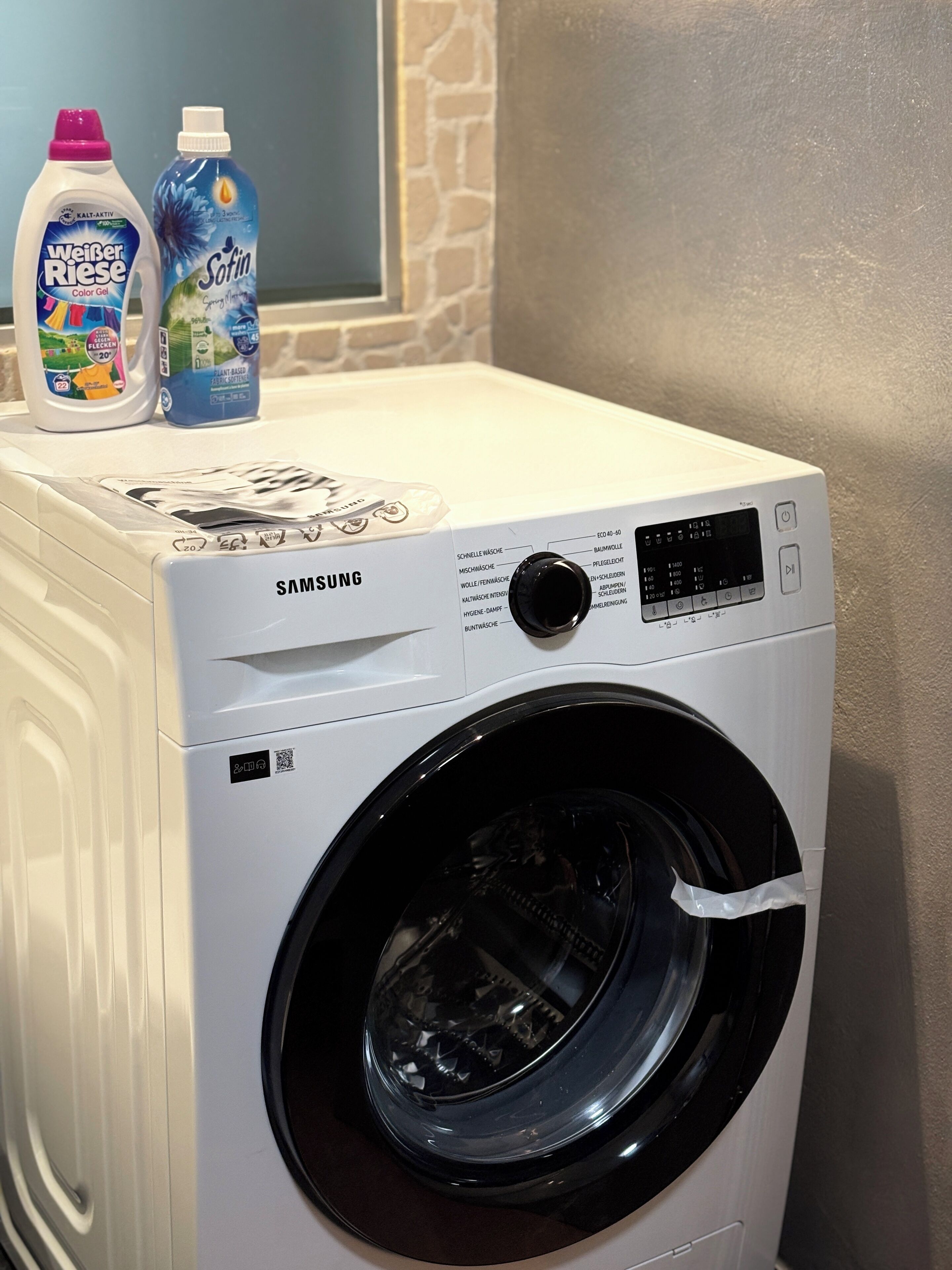 A Samsung front-loading washing machine with a control panel and two detergent bottles on top.