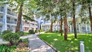 Un hotel de varios pisos con balcones, un camino pavimentado y abundante vegetación.