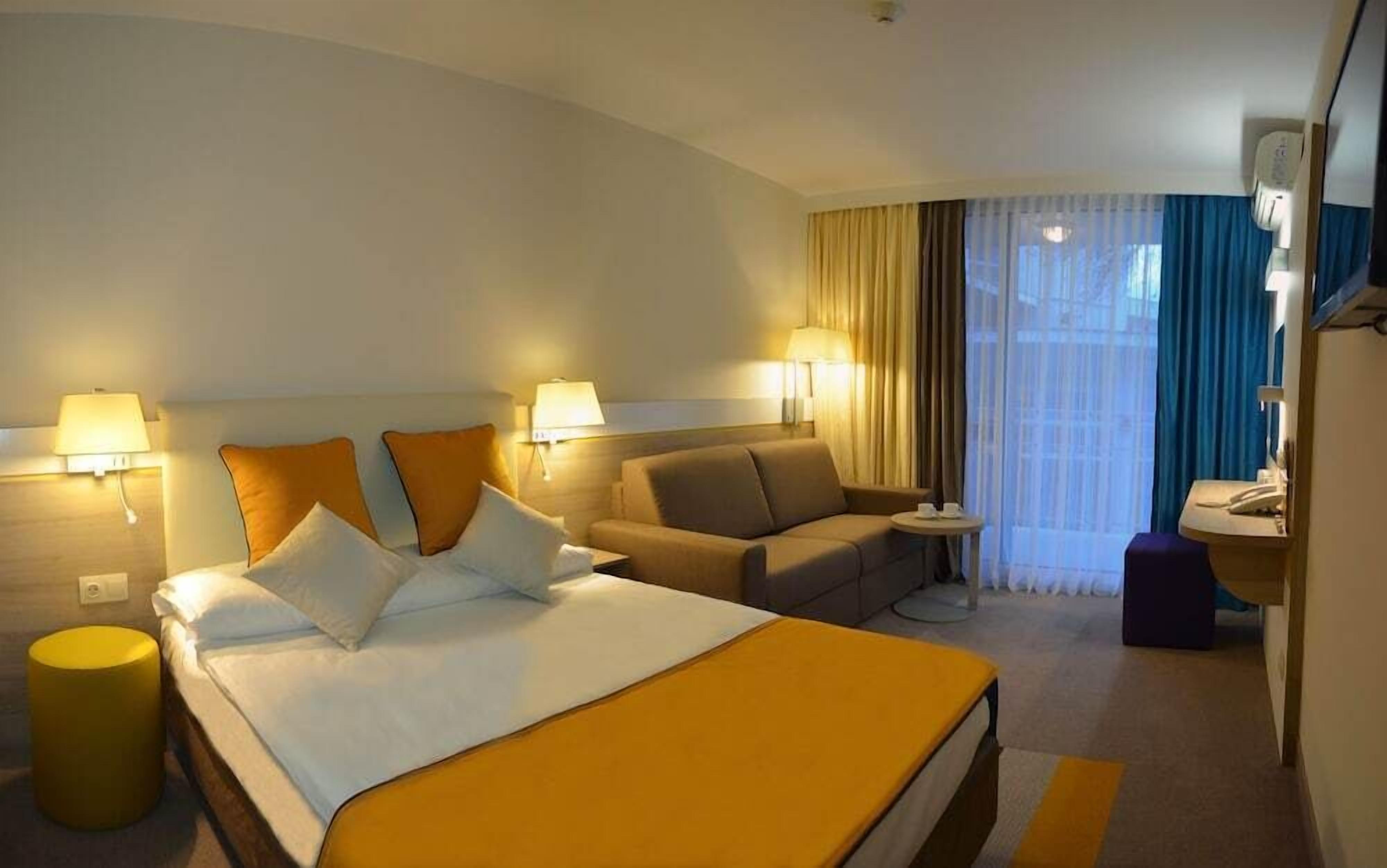 A hotel room with a bed, a sofa, a small table, a chair, and a bathroom area.