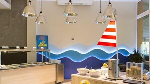 Un área de recepción con una pared con motivos de olas, una decoración de faro a rayas y un mostrador de buffet con diferentes alimentos.