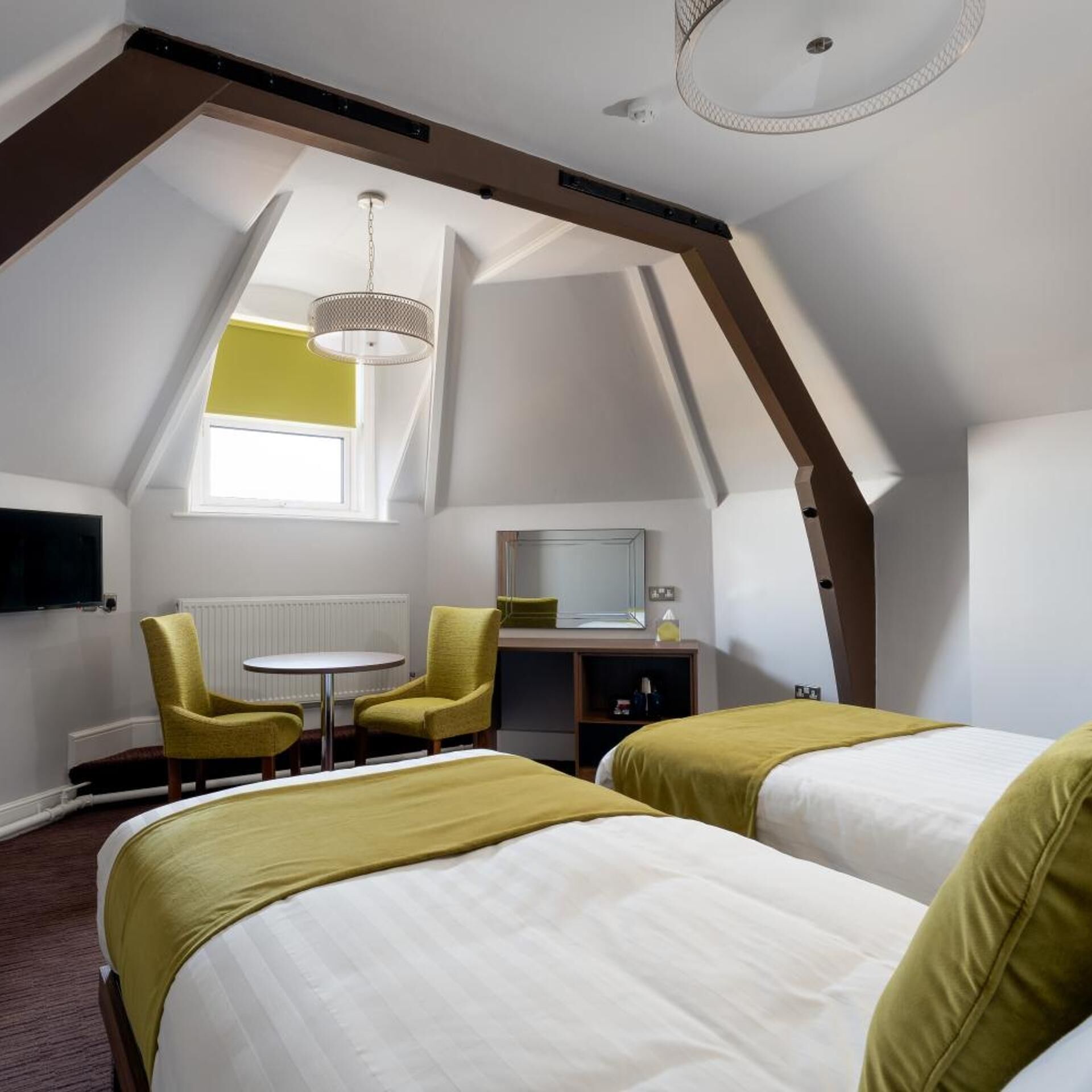 A hotel room with two beds, a small table, two chairs, a TV, and a window.