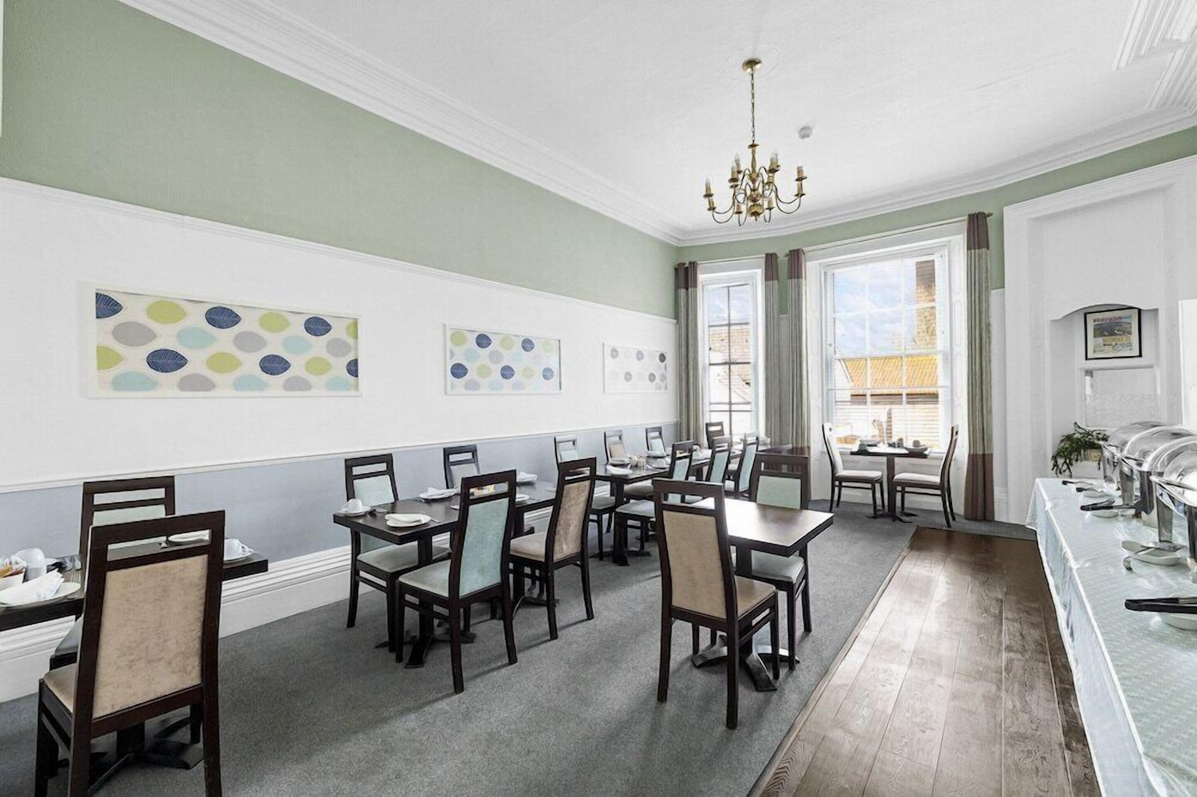 A dining area with multiple tables and chairs, a chandelier, and artwork on the walls.