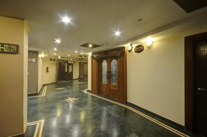 A hotel hallway with a fire exit sign, a wooden door with glass panels, and a star-patterned floor. - OYO Premium Nayapalli IRC Village (Bhubaneshwar)