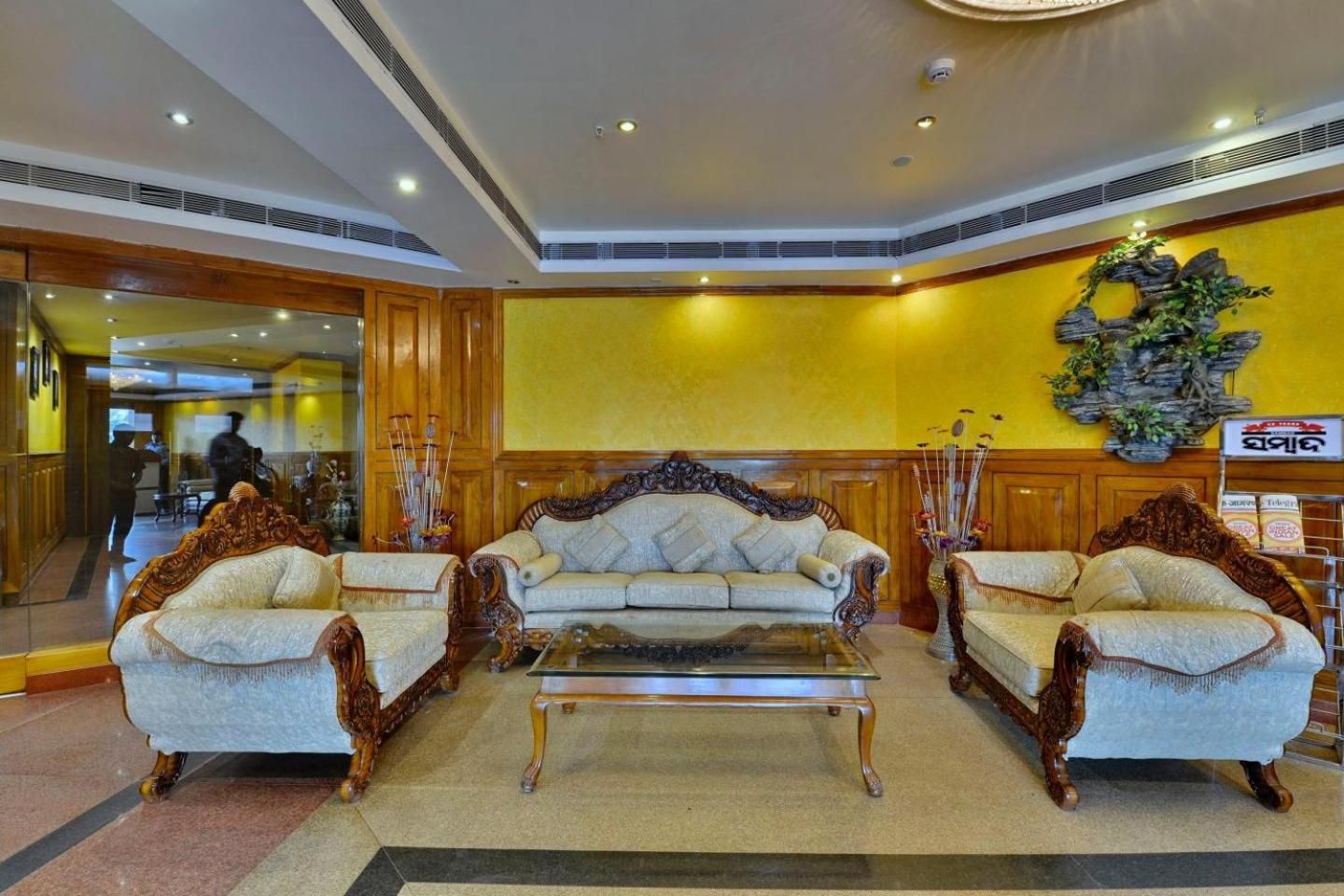 A lobby with two ornate sofas, a glass coffee table, and a decorative wall piece.