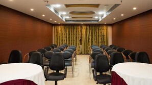 A conference room with rows of chairs facing a stage, a white table with a red tablecloth, and a curtain with a floral pattern. - OYO Premium Nayapalli IRC Village (Bhubaneshwar)