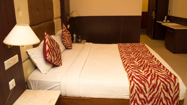A hotel room with a large bed, a bedside table, a lamp, and a nightstand. - OYO Premium Nayapalli IRC Village (Bhubaneshwar)