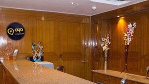 A hotel reception area with a wooden interior, a reception desk, and decorative vases with flowers. - OYO Premium Nayapalli IRC Village (Bhubaneshwar)