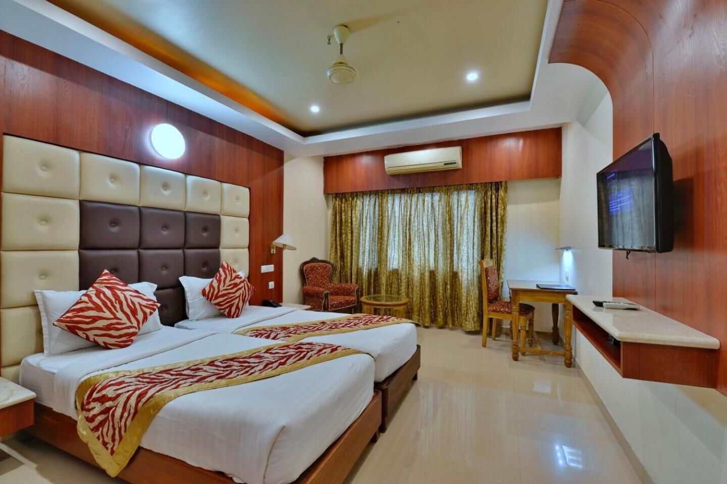 A hotel room with a large bed, a desk, a chair, and a television.