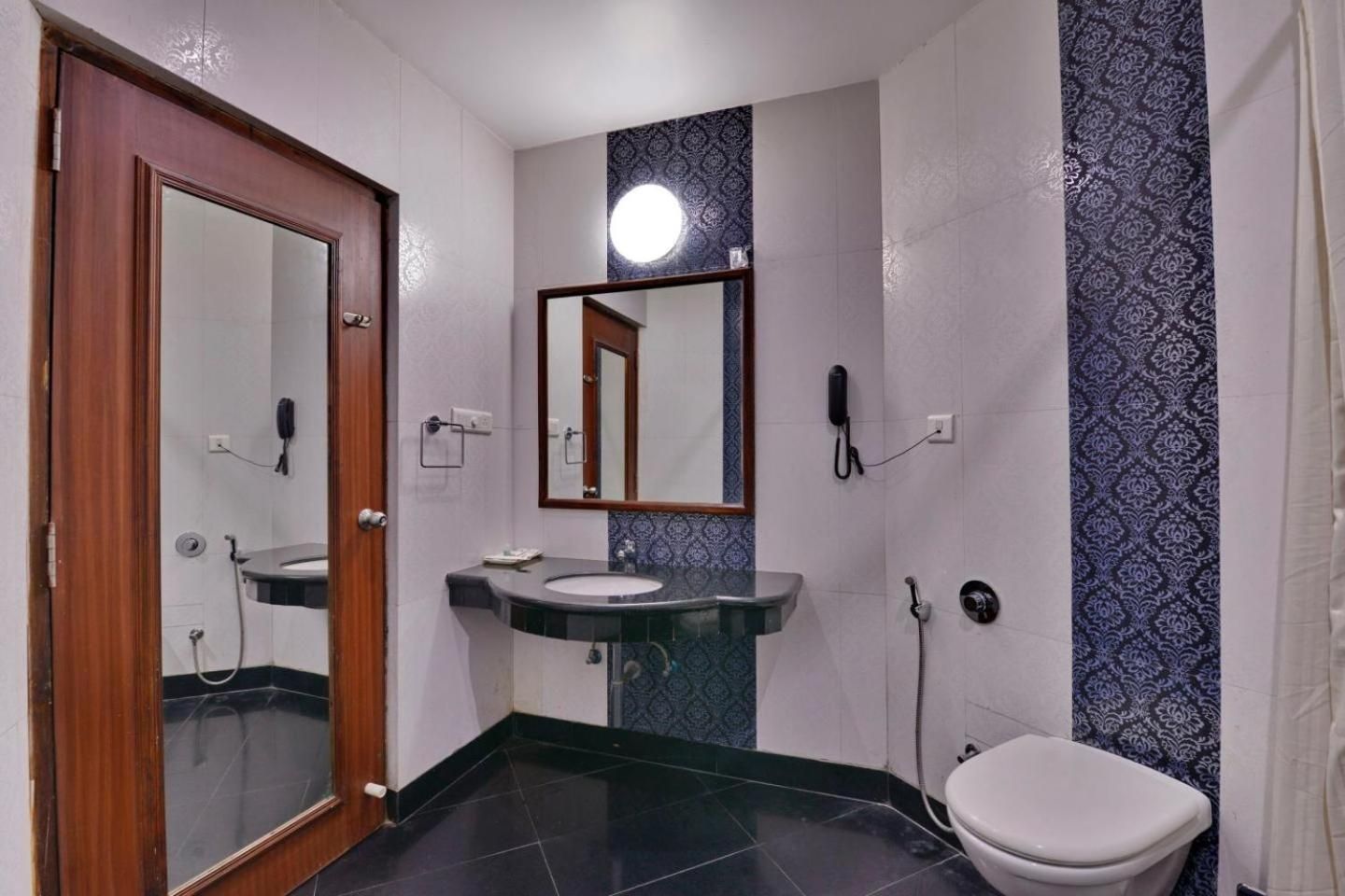 A bathroom with a wooden door, a sink with a mirror, a toilet, and patterned walls.