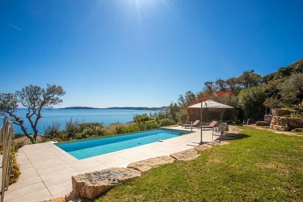 Ein Pool mit Blick auf das Meer, umgeben von einer Steinterrasse und einer Rasenfläche.