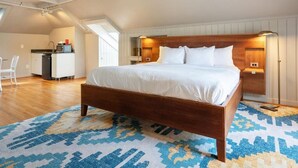 Ein Schlafzimmer mit einem hölzernen Bett, weißer Bettwäsche, einem gemusterten Teppich und einer kleinen Küchenzeile im Hintergrund.