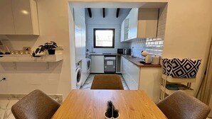 Une cuisine compacte avec des meubles blancs, une fenêtre et un coin repas comprenant deux chaises et une table.