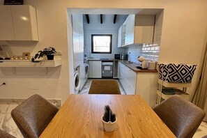 A compact kitchen with white cabinets, a window, and a dining area with two chairs and a table.