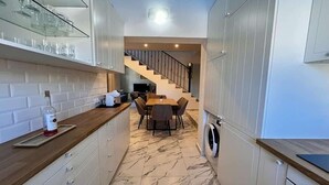 Une cuisine compacte avec des meubles blancs, un sol en marbre, un coin repas avec une table et des chaises, et un lave-linge.